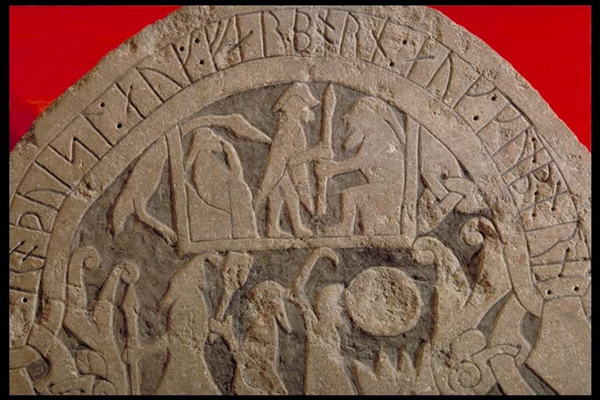 Detail of carving from Sanda churchyard, Gotland, potentially showing Valhalla, Odin, Frigg and an enormous duck. Frigg (seated, left) in a kubbstol (photo historiska.se CC BY 2.5 SE)