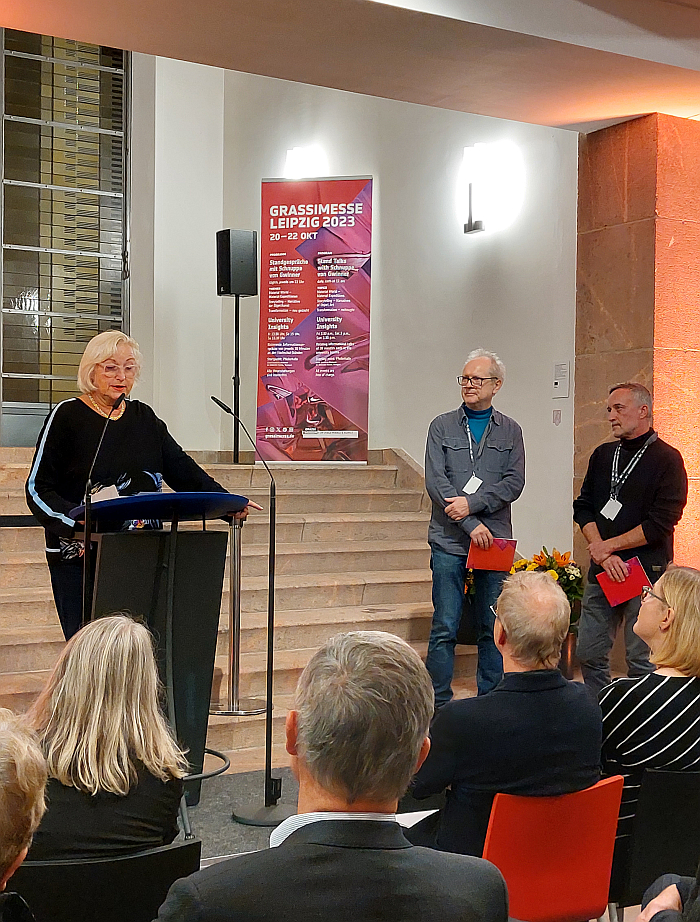 smow co-founder Martina Stadler reads the laudatio for Cornelius Réer (m) Annabella Hevesi / Line and Round IO (l, represnted by Gabor Bella) at the opening of the 2023 Grassimesse Leipzig